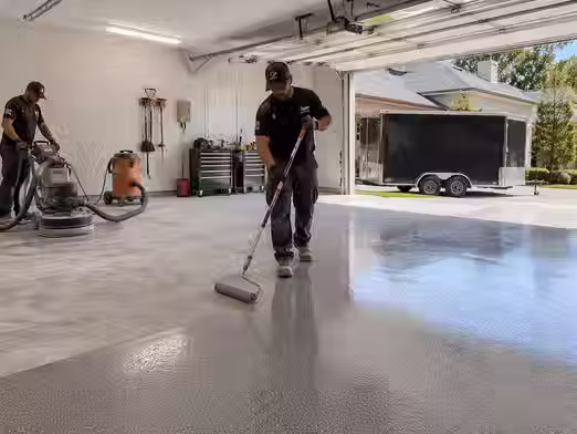 Professional contractor applying garage floor coating on concrete surface showing smooth epoxy finish and surface preparation work