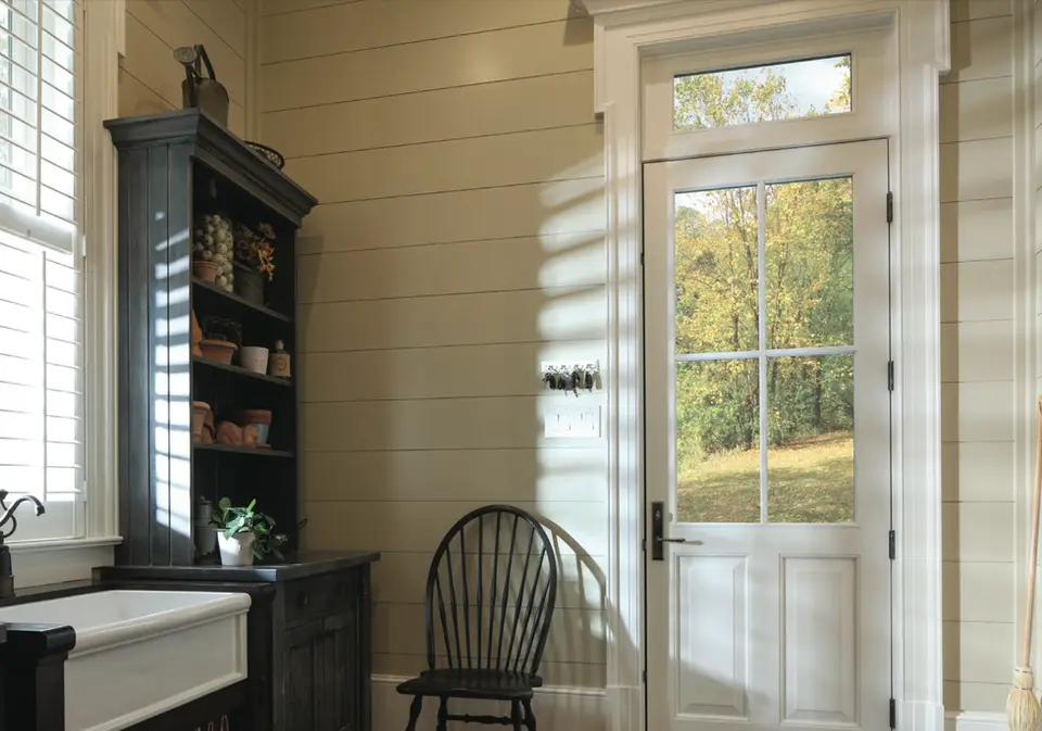 Sunlit room with wooden chair, shelves, and door showing autumnal landscape