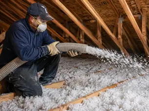 Technician installing blow-in insulation in a residential attic to improve energy efficiency and reduce noise.