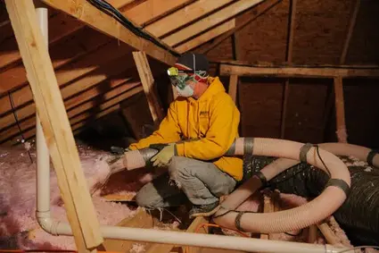 Worker installing pink insulation in attic