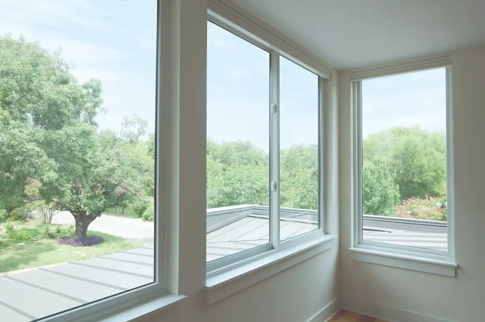 White sliding windows showcasing a lush green tree-filled landscape