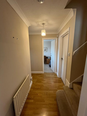 Bright hallway with warm neutral walls, white skirting boards, a radiator, and natural wood flooring.