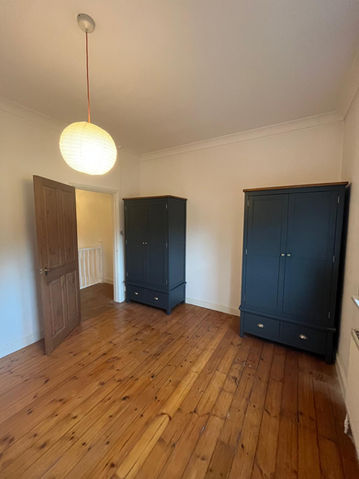 Bedroom with natural wood plank floors, light walls, and two dark Navy freestanding wardrobes.
