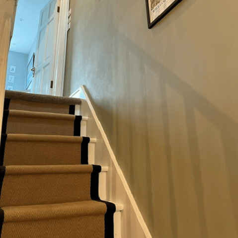 Wooden staircase featuring a neutral carpet runner with a bold black border and white painted spindles.
