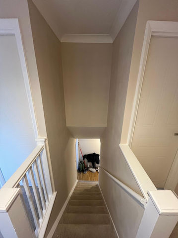 Looking down a carpeted staircase with white painted woodwork and neutral walls.