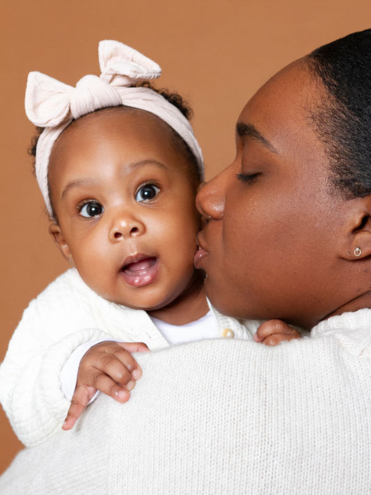 family photoshoot, mother kissing baby on the cheek, baby wearing white and a pink hair bow