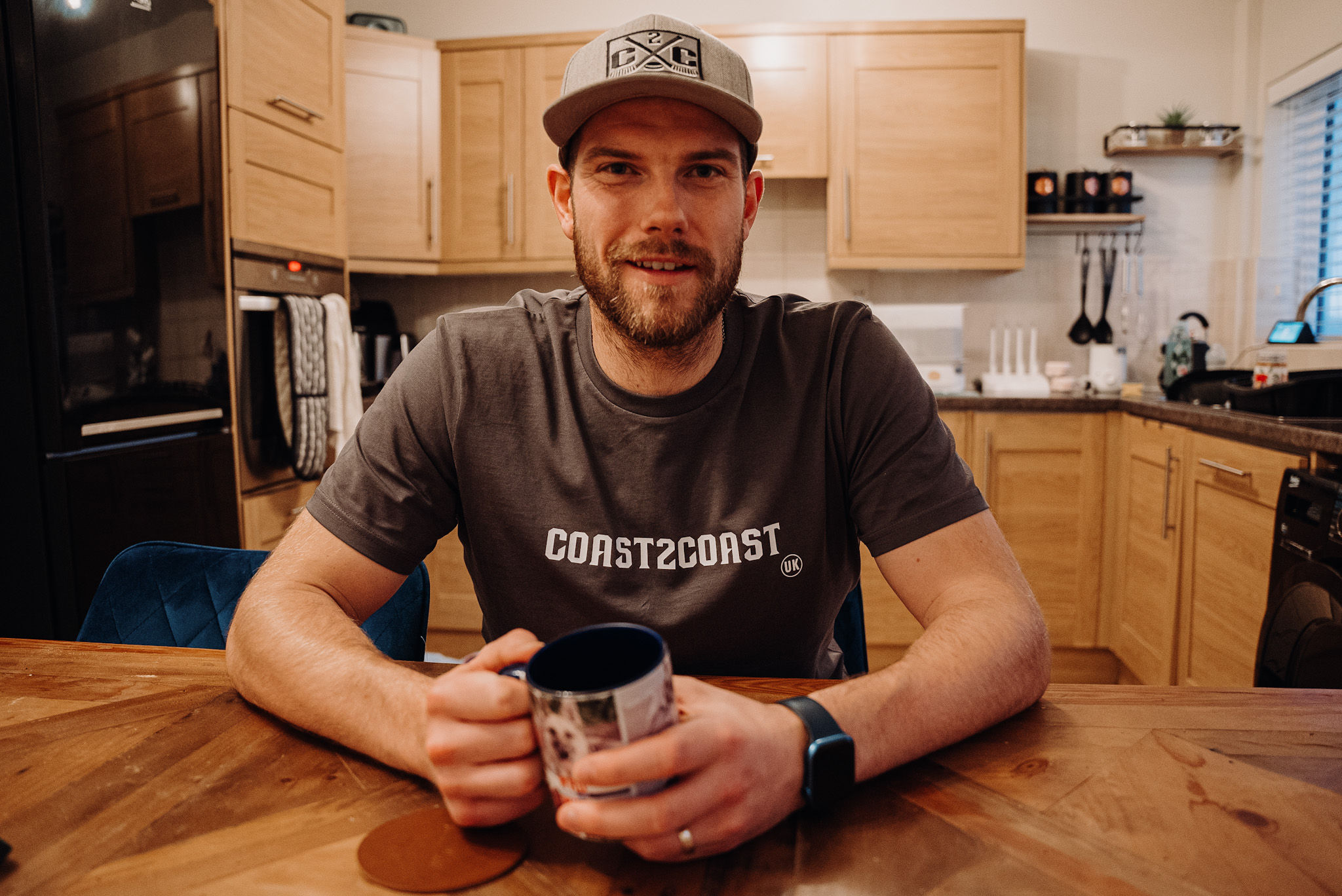 Ben Bowns drinking coffee in his kitchen wearing a coast 2 coast T-shirt