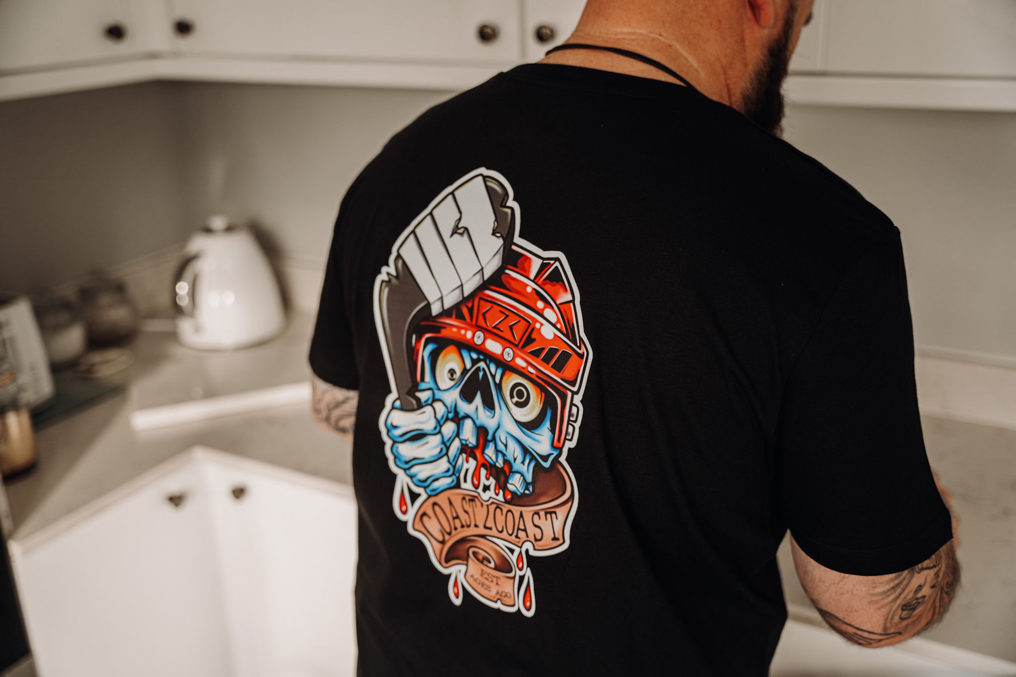 Stubob making a cup of coffee, wearing a black t-shirt with the crazy skull design on the back.
