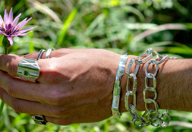 Handcrafted silver bracelet worn on wrist among green plants, featuring organic chain links