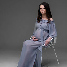 Schwangere Frau auf einem Stuhl in elegantem Kleid – modernes Babybauchshooting im Fotostudio Düsseldorf