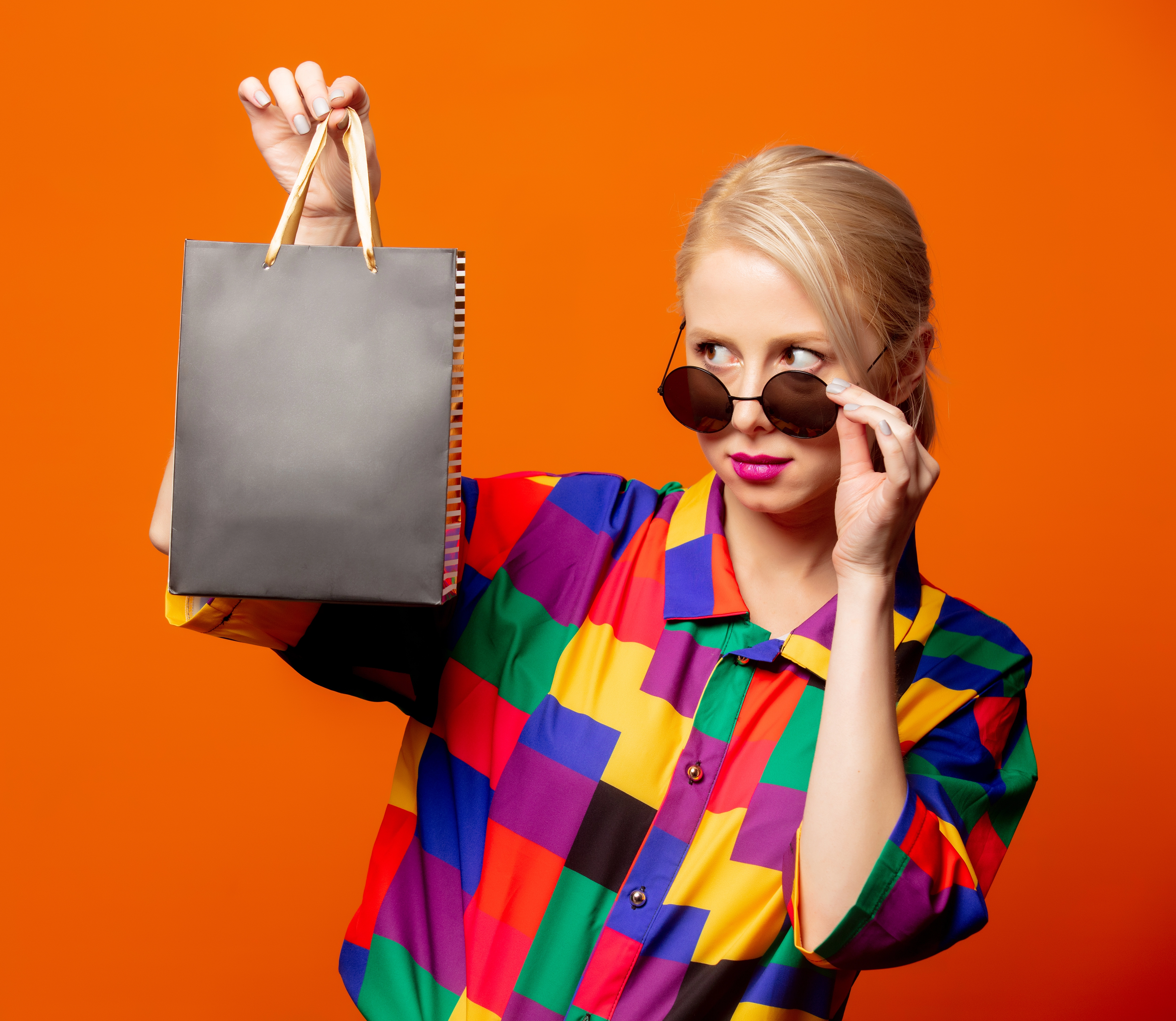 Portrait einer stilvollen Frau mit Sonnenbrille und Einkaufstüte vor orangenem Hintergrund – Studiofotoshooting