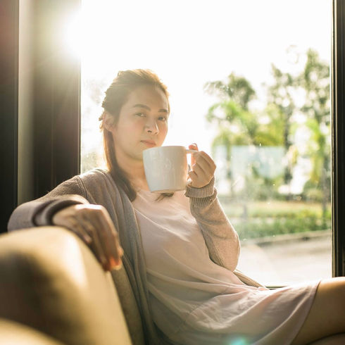 Vertical lifestyle portrait of a woman with a coffee mug in soft window light