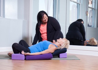 Yoga teacher Heather helping prop up a students in a restorative fish and bound angle pose