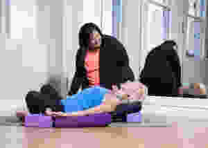 Yoga teacher Heather helping prop up a students in a restorative fish and bound angle pose