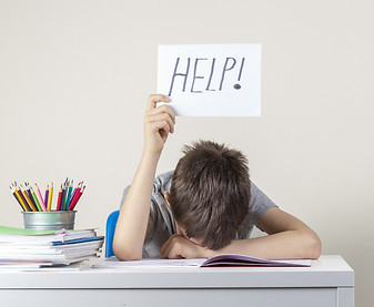 A child with his head on the table holding up a help sign