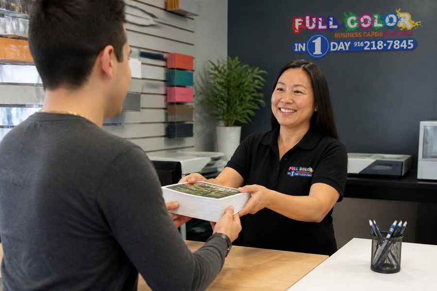 Friendly staff member handing a stack of printed flyers to a customer at a local print shop counter
