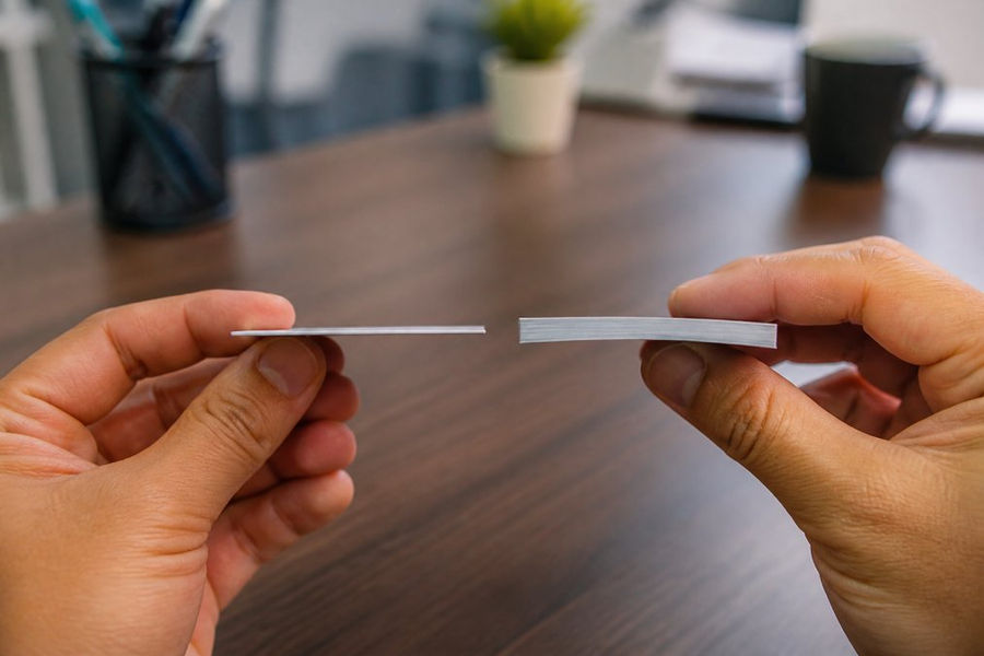 Close-up of hands holding two business cards side by side, one thin and flimsy, one thick and rigid, on a clean desk with natural lighting