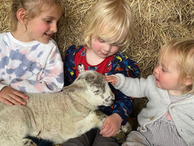 three young children petting a lamb with hay bales behind them