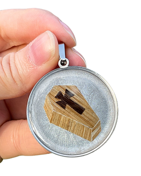 Coffin made with 2 hair colors, on a colored background, enclosed in resin in a silver-colored stainless steel pendant.