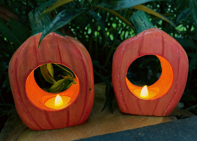 Two wood carvings shaped like pumpkins with a hole in the middle to hold tealights