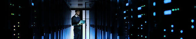 Person monitoring servers in a dark, glowing data center with a tablet.