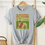 Thumbnail: Short sleeve grey shirt with vintage book cover of The Wizard of Oz in pale gold with grass green and red font