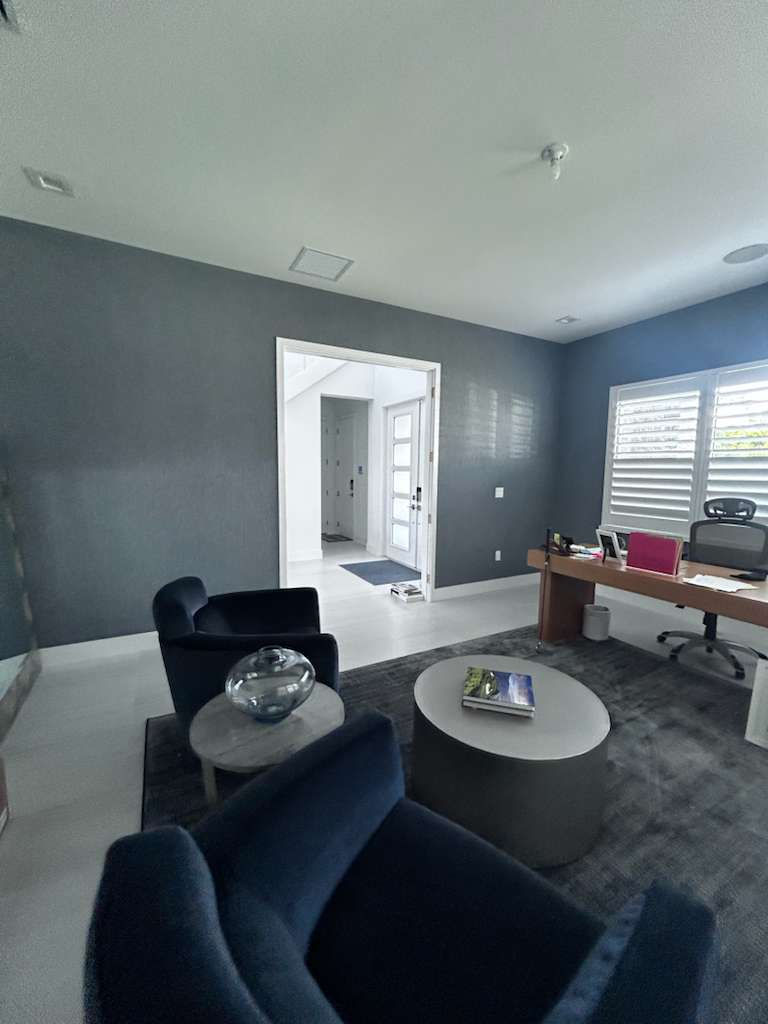 Modern office with blue chairs, a wooden desk, and a round table. Bright light from windows, grey walls, and a book on the table. Calm mood.
