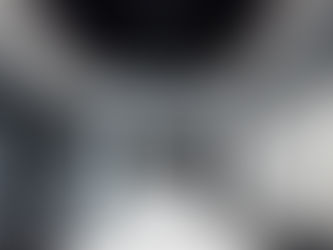 Modern conference room with a long white table, black chairs, and a wall-mounted TV. Glass wall reveals greenery outside. Black ceiling vents.