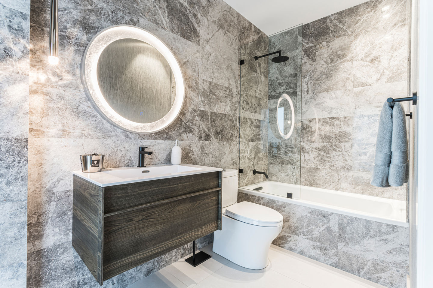 Modern bathroom with gray stone tiles, floating vanity, and circular mirror