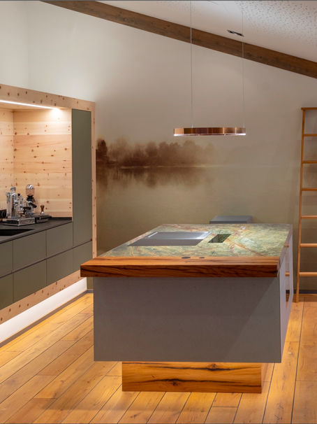 Modern kitchen with a wooden island, green cabinets, and a waterfall backsplash. A ladder leans against a wall. Warm lighting creates a cozy feel.