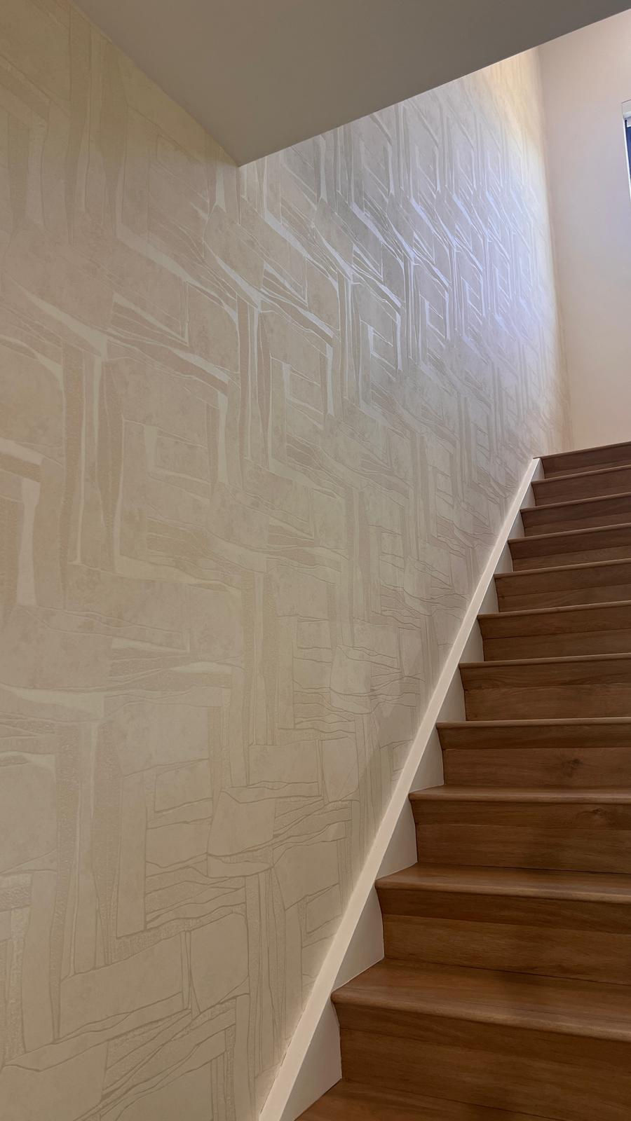 Two-story staircase wall in a Miami home on 9th Place installed with GUH56717 champagne geometric textured wallcovering alongside warm wood steps and white stair trim.