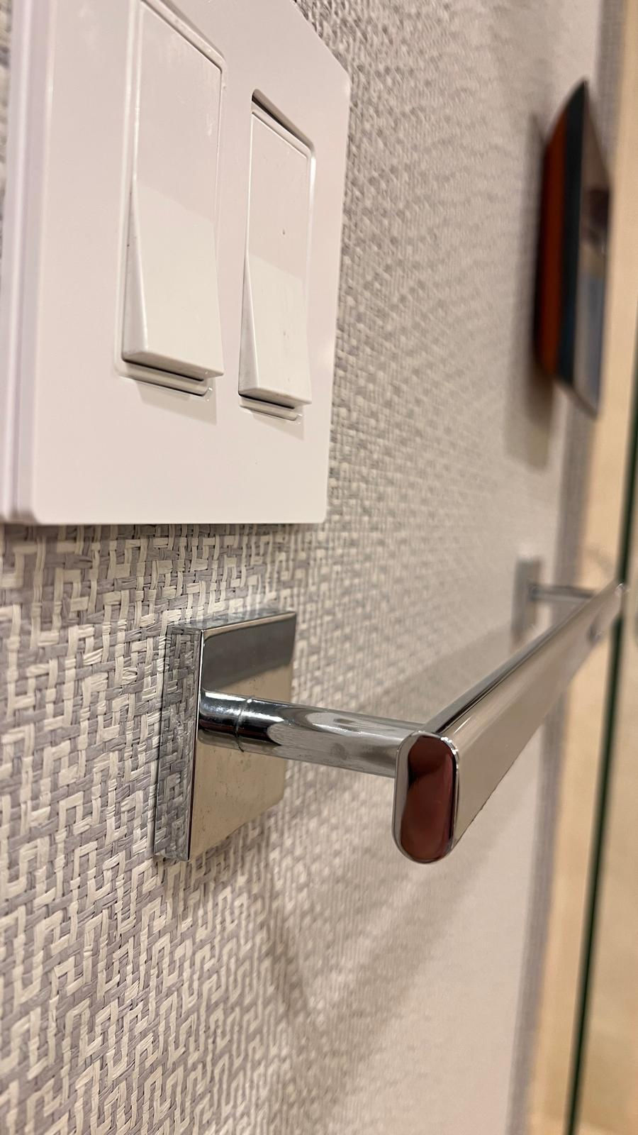Close-up of two white light switches on a textured wall, with a chrome towel bar below. Neutral tones create a clean, modern feel.
