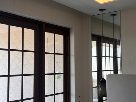Bedroom suite on Fisher Island with DYW103403 textured wallcovering framing dark wood french terrace doors, floor-to-ceiling mirror, and warm LED cove ceiling lighting designed by Guimar Urbina Interiors.