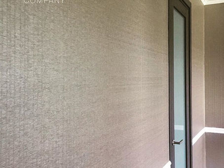 Textured beige wallpaper on hallway walls with a wooden-framed door. Text reads "The Wallpaper Company." Bright, modern atmosphere.
