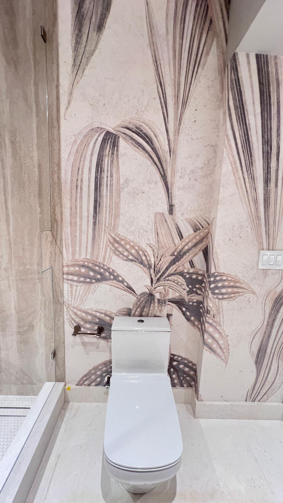 White toilet against a beige wall with large leaf patterns. A shower stall is on the left. Luxurious and modern bathroom setting.