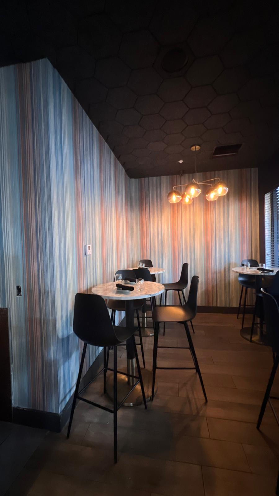 Precise corner alignment of a vertical striped custom mural wallpaper installed at Korner67 in Miami Lakes, showing the transition between the dining room nook and the service bar area.