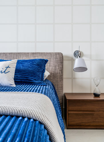 Blue bedding, wall lamp, and nightstand in bedroom