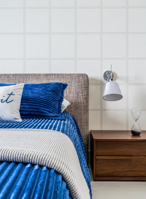 Blue bedding, wall lamp, and nightstand in bedroom