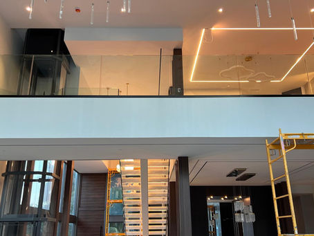 Modern interior with glass staircase, suspended lighting, and an under-construction area featuring scaffolding. Sleek and contemporary design.