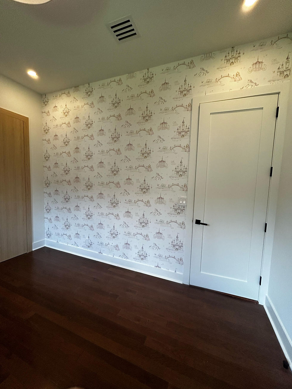 Room with white walls and dark wood floor, featuring a patterned wallpaper of castles and carriages. Closed white door, ceiling lights on.
