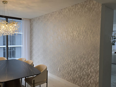 Modern dining room with tree-patterned wallpaper, black table, beige chairs, and a crystal chandelier. Large windows show cityscape view.