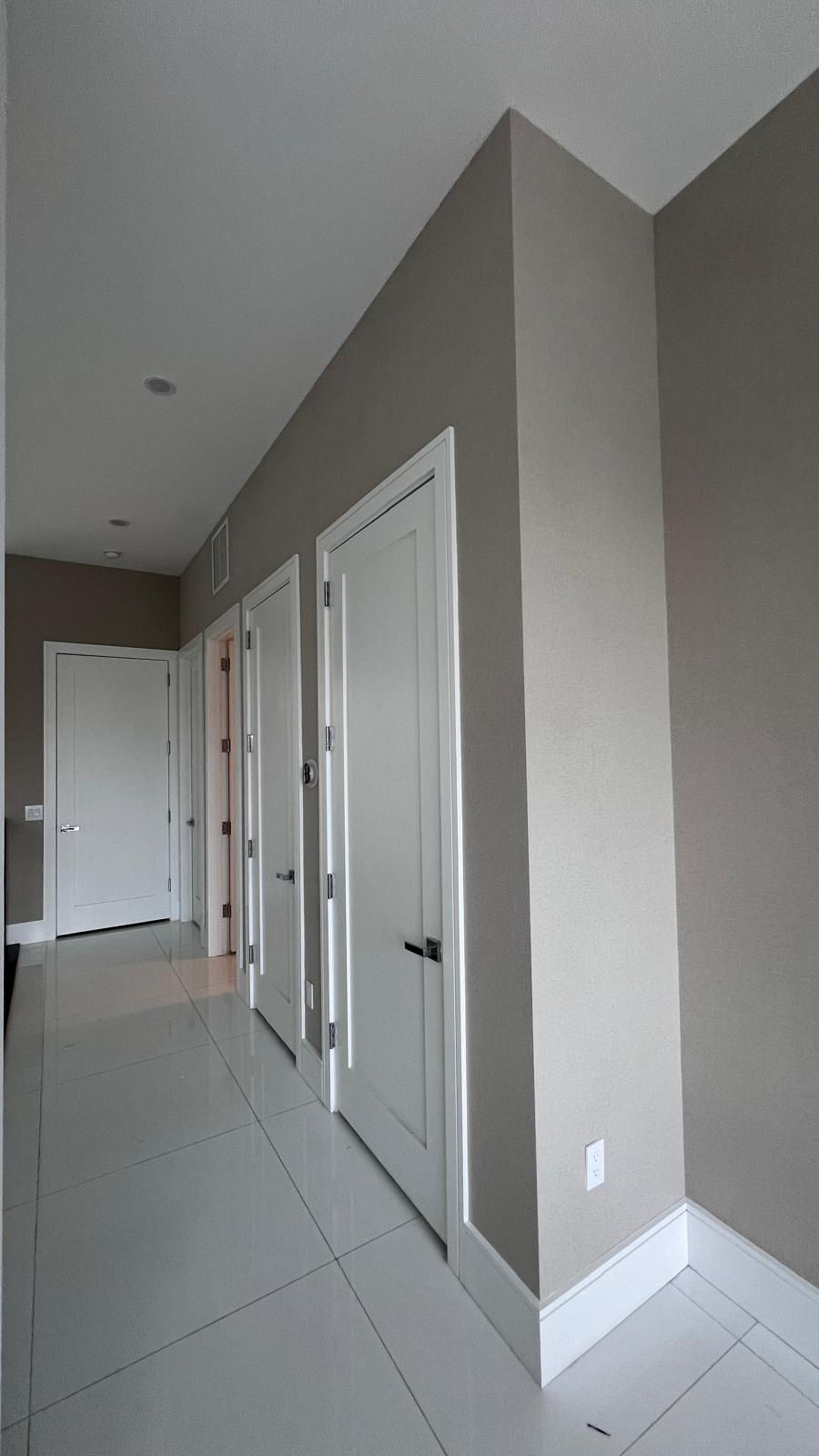 High-traffic hallway in a North Miami Beach home installed with GUH42225 metallic taupe textured silk wallcovering around white door frames and polished tile floors.