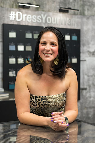 Woman smiles, leaning on a table, in front of a wall with #DressYourself text.