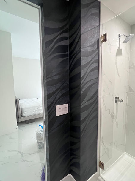 Modern bathroom with black wave-patterned wallpaper, marble tiles, and walk-in shower. Bedroom visible through the open door.