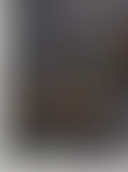 Wooden table with open book, abstract gold sculpture, and white flower in vase. Dark textured wall background, modern and minimalist.