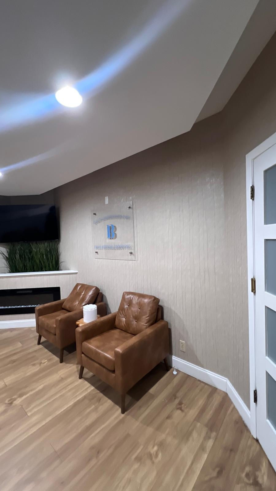 Belle Medical Group reception lobby in Boca Raton featuring SHO18007 taupe vertical textured commercial wallcovering behind a floating acrylic company sign and cognac leather armchairs.