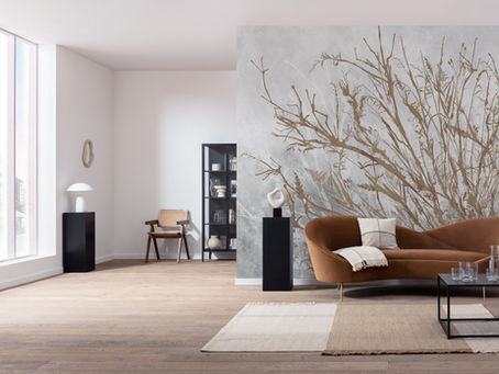 Minimalist living room with a brown sofa, plant wall art, and glass coffee table. Neutral tones, large window, and cozy atmosphere.