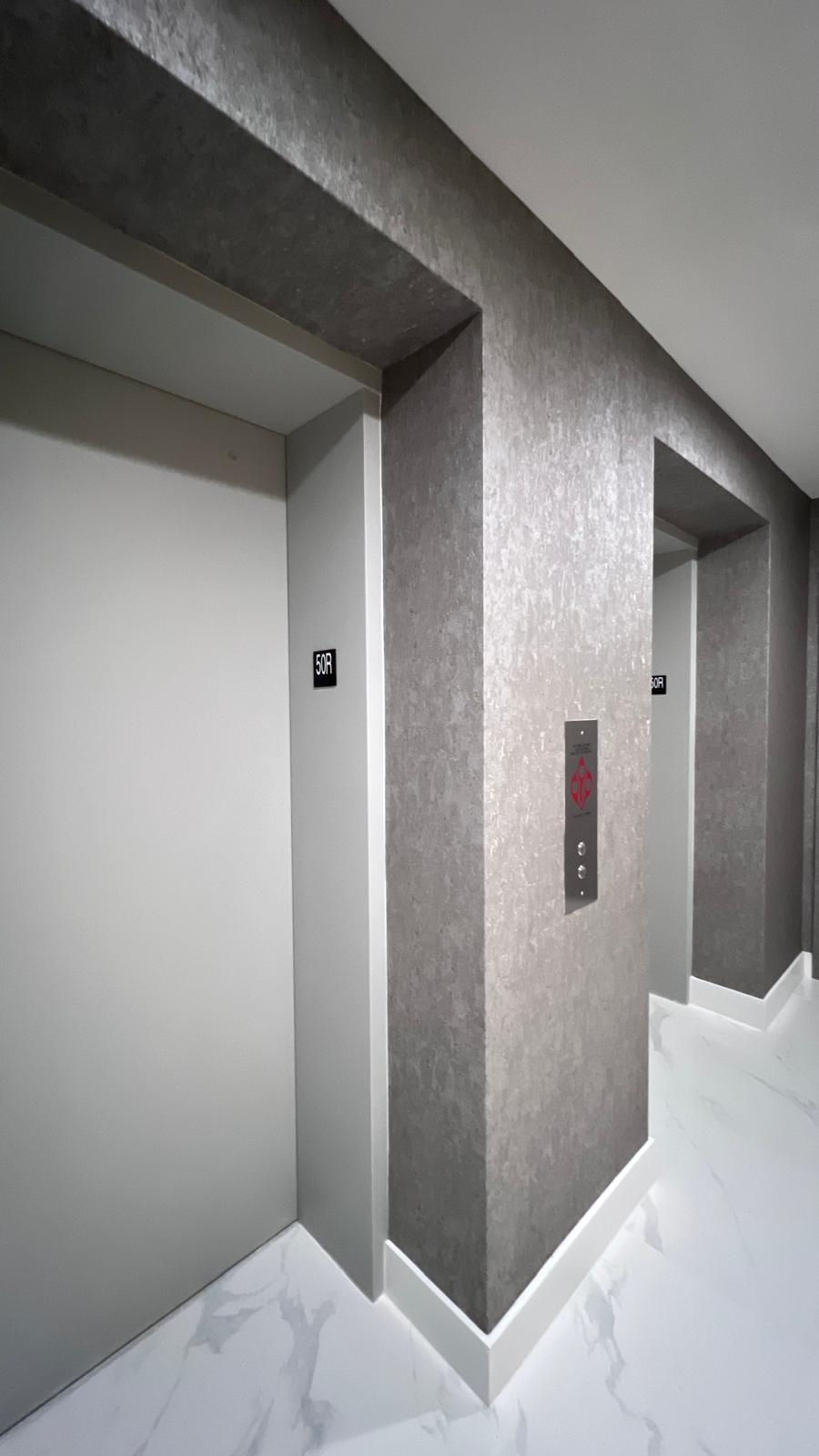 Gray elevator doors in a modern hallway, floor indicator shows "50R". Marble-patterned floor enhances clean, sleek design.