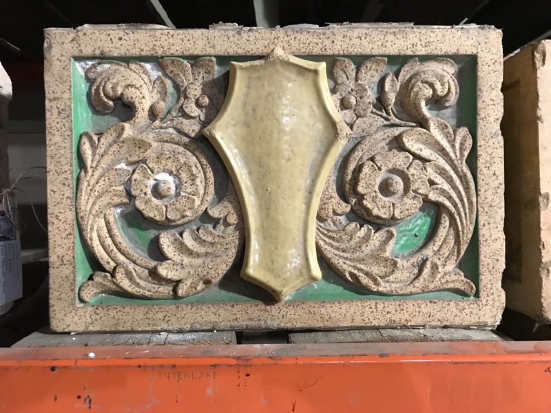 Terra Cotta shield in floral field with polychrome glaze, in green and gold.