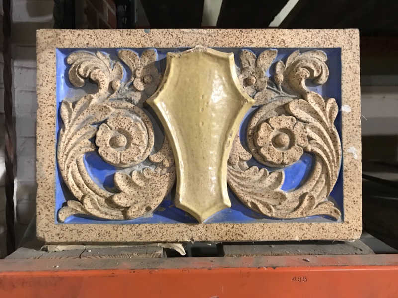 Terra Cotta shield in floral field with polychrome glaze in gold and blue.